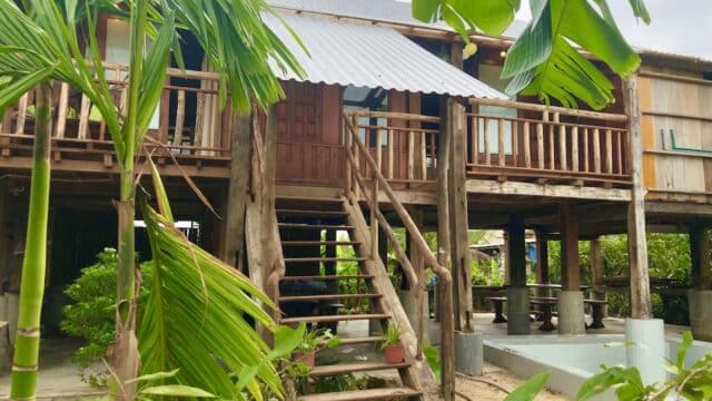 A rustic wooden house on stilts in Hoi An, surrounded by lush tropical plants and trees.
