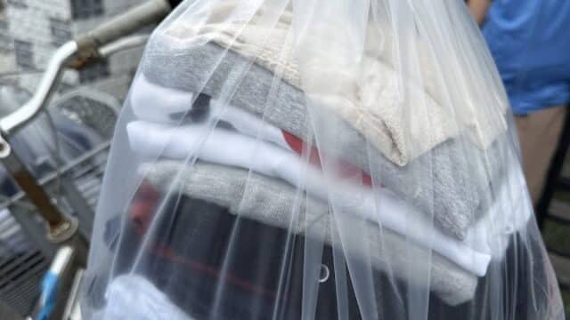 A plastic bag filled with folded clothes hangs from a bicycle handlebar outdoors in Hoi An.
