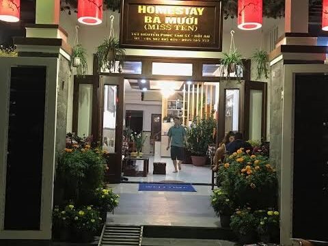 Entrance of Homestay Ba Mươi in Hoi An at night, with plants, red lanterns, and a motorbike parked outside.