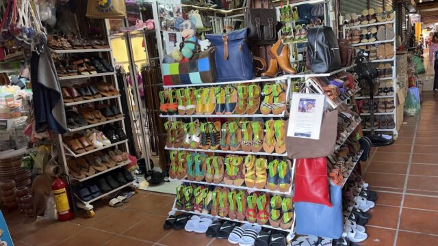 A market stall in Hoi An displaying rows of colorful sandals, shoes, and bags on racks and shelves.