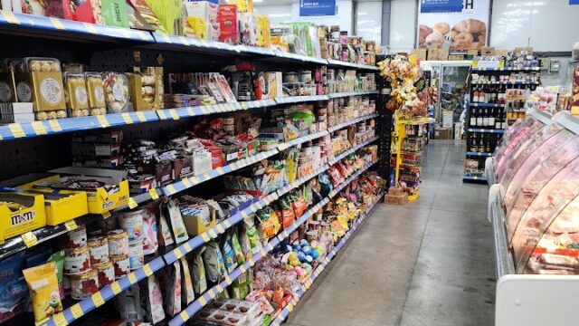 A grocery store aisle in Hoi An with shelves of snacks, candy, and food items; refrigerated section on the right.