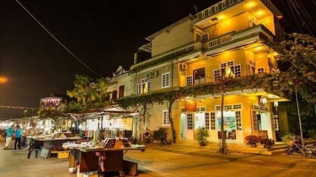 A warmly lit building and outdoor market stalls at night on a quiet street in Hoi An.