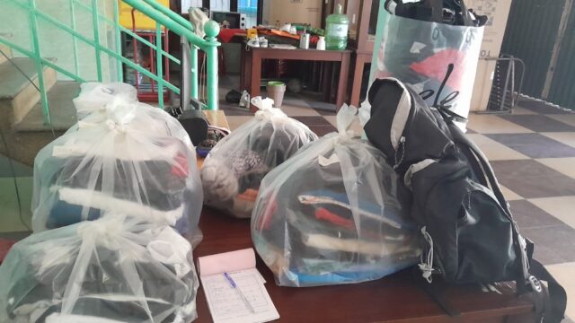 Four bags and a backpack filled with clothes sit on a table indoors near stairs and boxes, ready for a trip to Hoi An.
