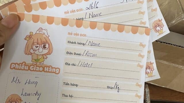 Three illustrated order receipts with handwritten details, held over a box in a cozy Hoi An setting with wooden chairs and a hand in the background.