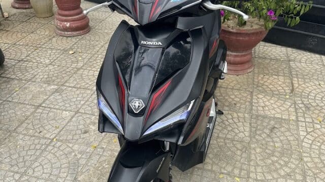 A black Honda motorbike with red accents parked on a tiled area near potted plants in Hoi An.
