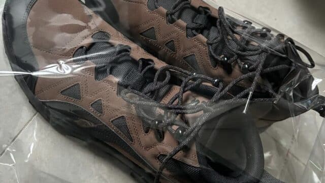 A pair of brown and black Hoi An sneakers with black laces inside a clear plastic bag on a gray surface.