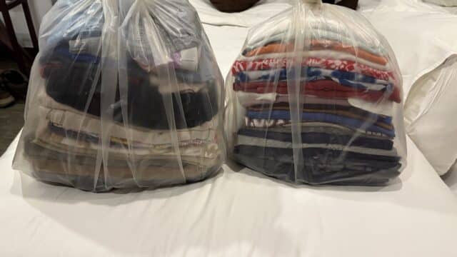 Two large plastic bags filled with neatly folded clothes, reminiscent of a laundry day in Hoi An, placed on a white bed.