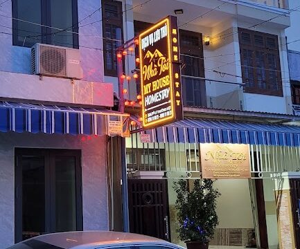 A silver car is parked before a three-story building in Hoi An with signs reading My House Homestay in Vietnamese and English.