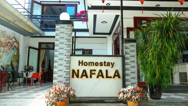 Entrance of Homestay NAFALA in Hoi An, featuring a large sign, potted plants, lanterns, and an inviting outdoor seating area.
