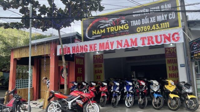 A row of motorcycles is parked outside Nam Trung in Hoi An, with Vietnamese signs hanging above the entrance.