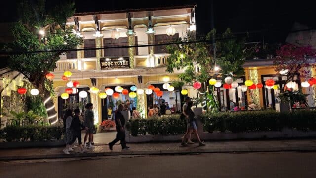 People walk by a brightly lit Hoi An restaurant, colorful lanterns glowing outside and lighting up the night.