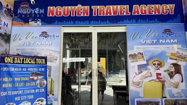 Front view of NGUYEN TRAVEL AGENCY with posters of Hoi An and smiling tourists holding luggage.