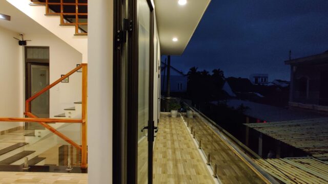Modern house with a lit indoor staircase and a balcony overlooking Hoi An’s charming neighborhood at night.