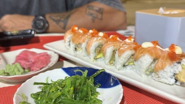 A plate of sushi rolls, seaweed salad, and wasabi on a red table in Hoi An with a person sitting in the background.
