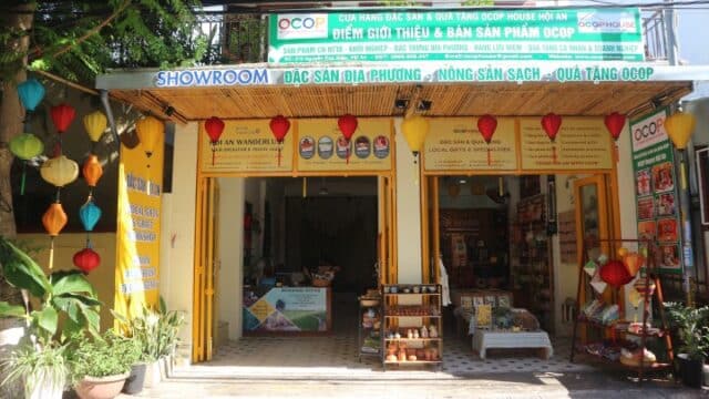 A yellow Hoi An storefront with colorful lanterns, banners, and shelves displaying local specialty products.