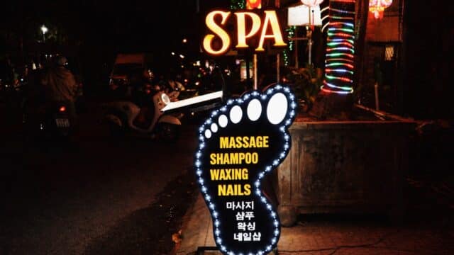 Illuminated foot-shaped spa sign in Hoi An advertises massage, shampoo, waxing, nails with text in English and Korean.