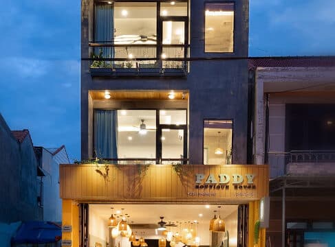 A modern three-story building in Hoi An with a bright, inviting café on the ground floor, lit warmly in the evening.