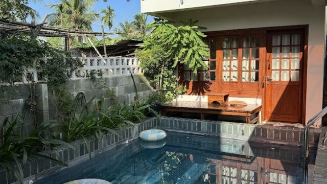 Small Hoi An backyard pool with floaties, lush plants, brick walls, and a balcony overlooking from the two-story house.