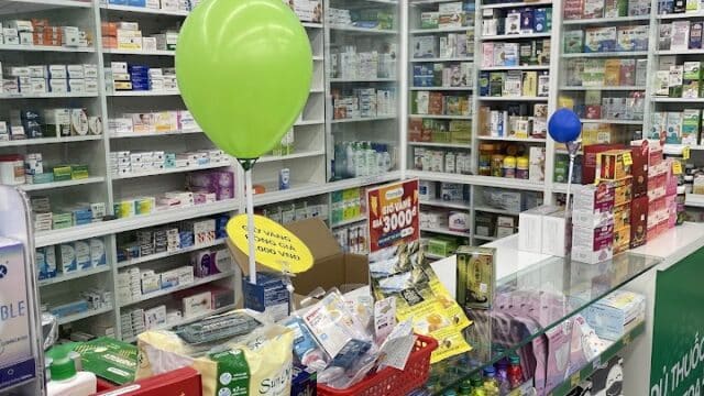 A pharmacy counter in Hoi An with medicine shelves, a green balloon, and various products and promotional signs on display.