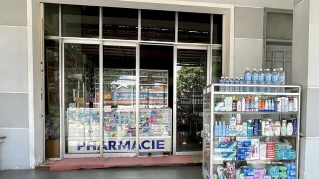 A pharmacy entrance in Hoi An with glass doors and a cart outside displaying bottled water, hygiene, and health products.