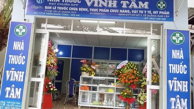 Pharmacy storefront in Hoi An with blue signage reading Nhà Thuốc Vĩnh Tâm, floral displays by the entrance.