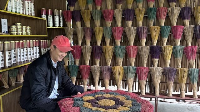 A person arranges colorful incense sticks in Hoi An, displaying them in bundles on a table and hanging on a wall.