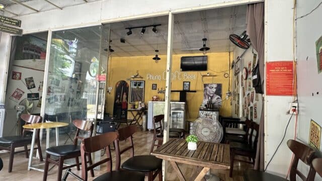 Small, cozy cafe in Hoi An with wooden tables, chairs, yellow walls, and vintage decor, viewed from the entrance.