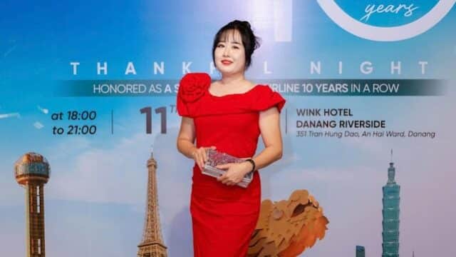 Woman in a red dress stands holding an award before an EVA Air 10th anniversary backdrop, evoking the elegance of Hoi An.