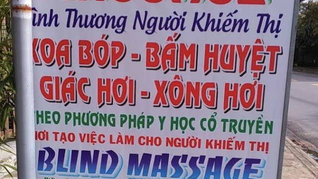 A sign in Hoi An advertises a blind massage service in Vietnamese and English beside the road.