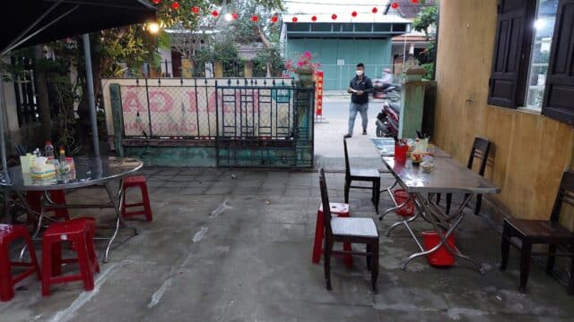 Outdoor restaurant in Hoi An with empty tables, condiments, and one person standing near the entrance in the background.