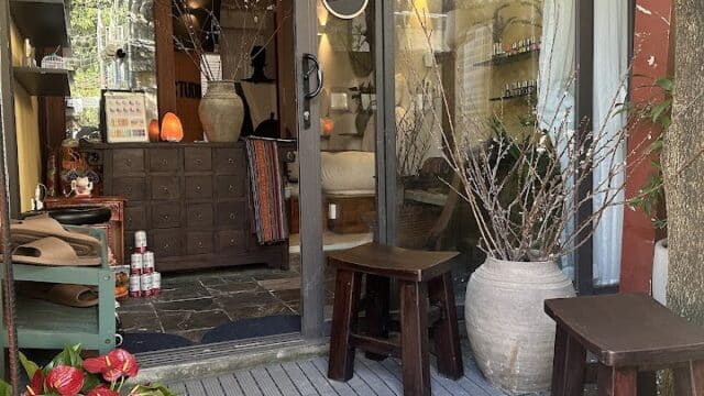 A cozy Hoi An shop entrance with plants, stools, large pots, and an OPEN sign. Warm interior lighting glows through the glass door.