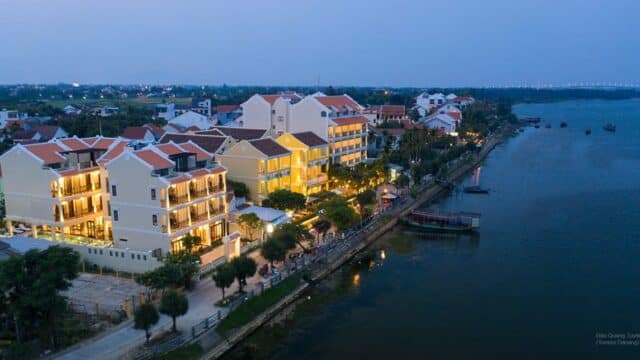 A riverside town at dusk with lit buildings, waterfront walkways, and boats along the calm water in enchanting Hoi An.