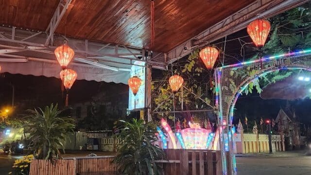 An outdoor Hoi An restaurant at night with red lanterns overhead and empty tables and chairs, creating a tranquil scene.