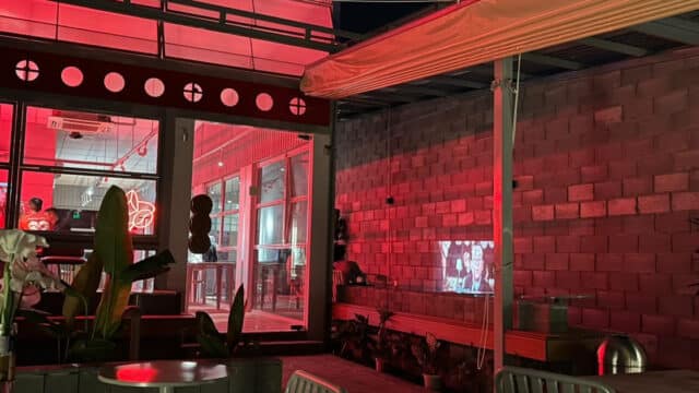 Outdoor patio in Hoi An with tables, red lighting, and a movie projected onto a brick wall at night.