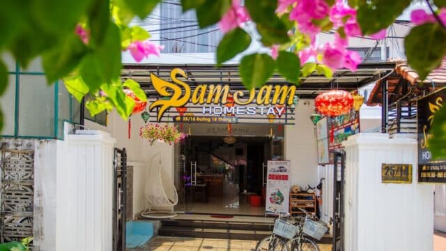 The entrance of SamSam Homestay in Hoi An features bicycles, flowers, and a bright, welcoming sign.