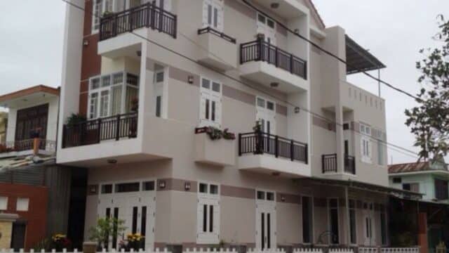 Three-story modern house with balconies, white fence, and large windows on a corner street in vibrant Hoi An.