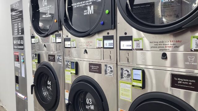 Four front-loading dryers stacked in Hoi An’s self-service laundromat, each door featuring clear instructions.