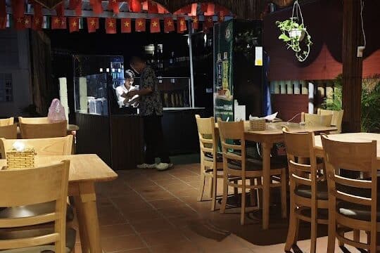 A cozy Hoi An restaurant with wooden tables, lanterns above, and a person standing at the counter in the background.