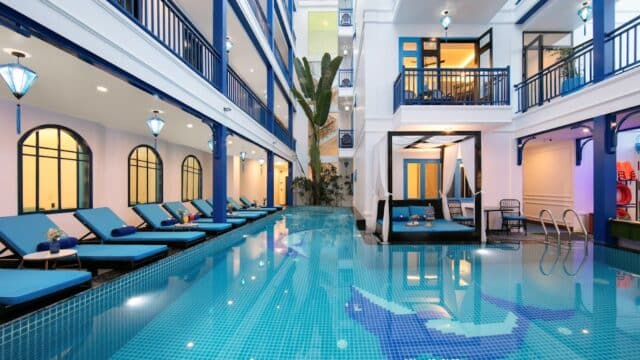 A modern Hoi An hotel courtyard with a pool, blue lounge chairs, balconies, and a tall cactus centerpiece.