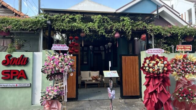 A spa entrance in Hoi An adorned with lush flower stands, signs, and greenery above its open wooden gate.