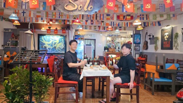 Two people dine at a table in vibrant Hoi An, surrounded by international and communist flags and eclectic wall art.