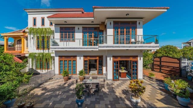 Modern two-story house with large windows, potted plants, and patio furniture reminiscent of stylish Hoi An homes.