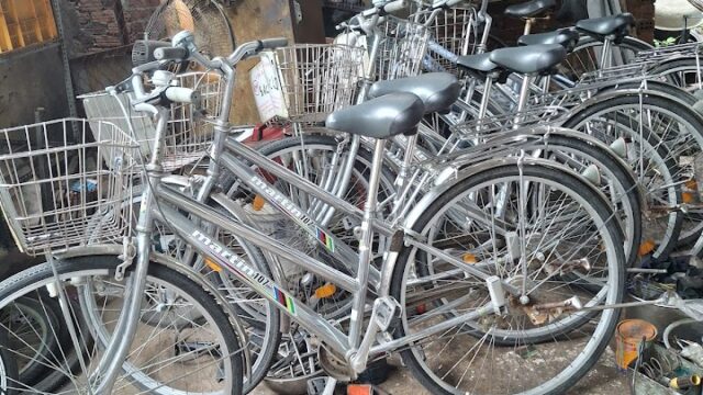 Several silver bicycles with baskets are parked closely in a workshop-like Hoi An space, surrounded by tools and debris.