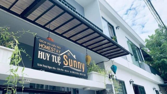 A modern white homestay building in Hoi An with a sign reading Huy Tuệ Sunny and hanging lanterns outside.