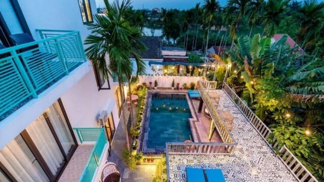 A vibrant courtyard with a pool, terrace, and tropical plants in Hoi An, viewed from above at dusk.