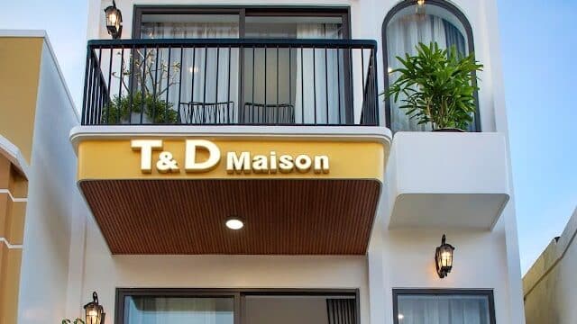 Three-story modern white building in Hoi An with balconies, plants, and a T & D Maison sign on the middle level.