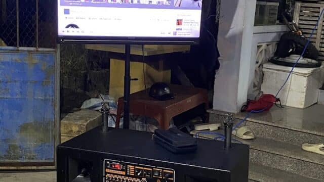A TV on a stand displays a YouTube video above a large speaker in Hoi An’s outdoor setting at night.