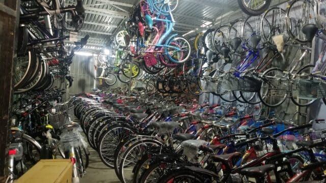 Dozens of bicycles, typical of Hoi An, are packed closely in a corrugated metal shed, with some hanging from the ceiling.