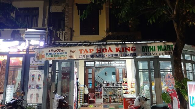 A brightly lit mini mart in Hoi An, Vietnam at night, with scooters parked outside and a sign above the entrance.