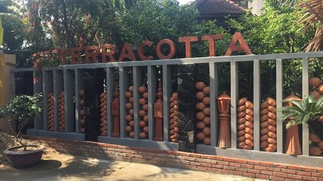 Terracotta-themed wall with decorative clay pots and a TERRACOTTA sign, inspired by Hoi An, in a garden setting.